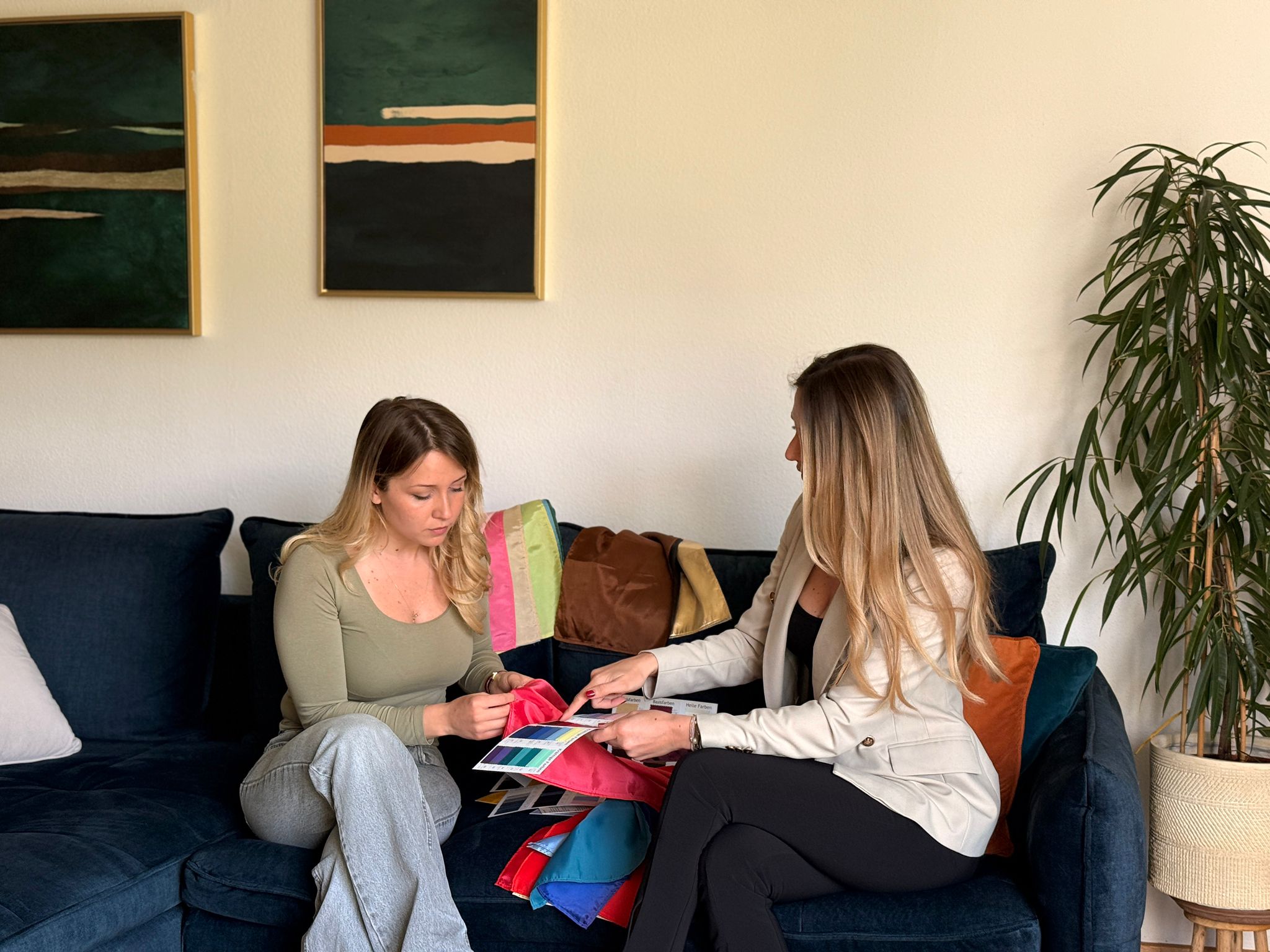 Stilberaterin und Kundin auf dem Sofa beim gemeinsamen Durchsehen von Farbkollektionen